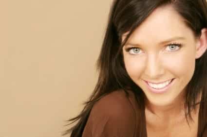 Woman smiling at camera against beige background, professional headshot for dental practice.