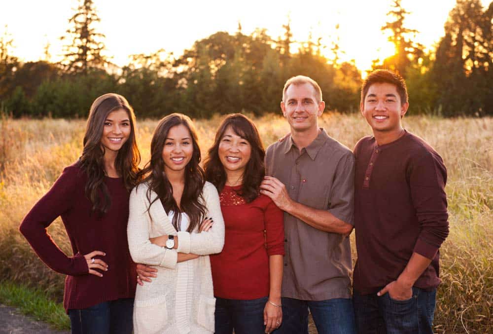 Five people smiling together in a golden field at sunset.