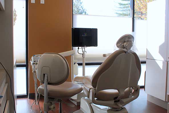 Modern dental office interior with two empty treatment chairs and monitor display on wall.