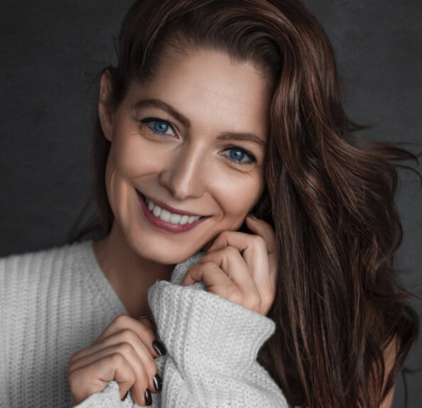 Woman smiling warmly at camera, wearing cream sweater, professional portrait for dental practice