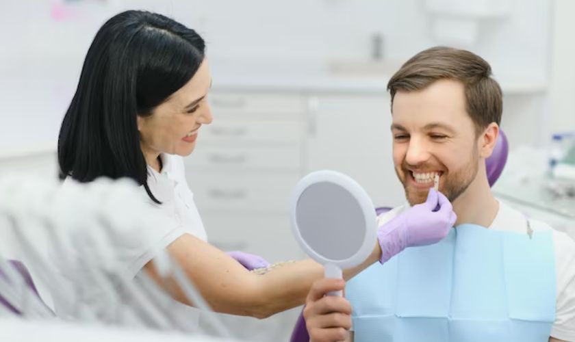 Dentist showing male patient his smile in mirror during dental checkup at clinic.
