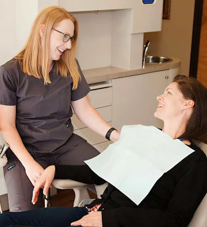 Dental hygienist consulting with patient holding paperwork in modern dental office treatment room.