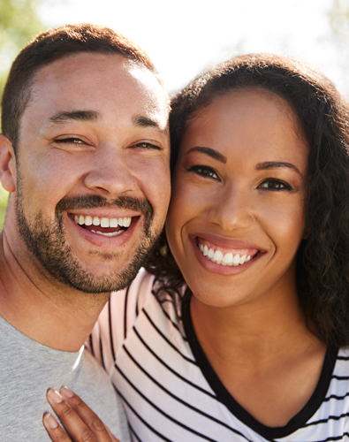 Happy couple smiling together outdoors in casual clothing, representing friendly dental care service.