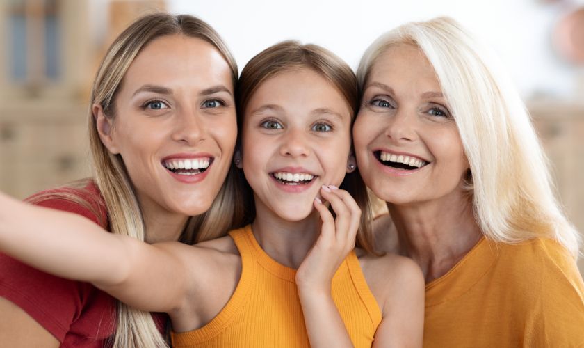 Three smiling women of different ages embracing together outdoors in warm clothing.