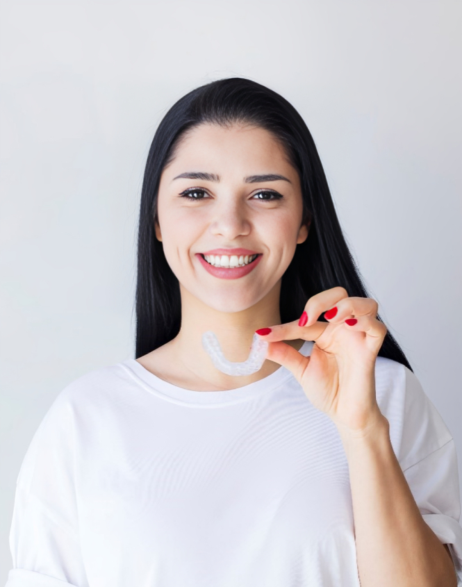 Young woman smiling while holding an invisible aligner, wearing white shirt against white background.