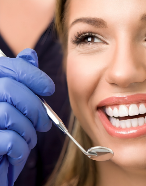Dentist in blue gloves examining smiling patient's teeth with dental mirror during checkup.