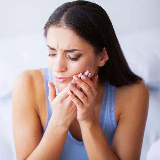Woman experiencing tooth pain, holding her cheek with concerned expression indoors.