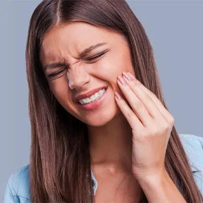 Woman experiencing tooth pain, touching her cheek against neutral background.