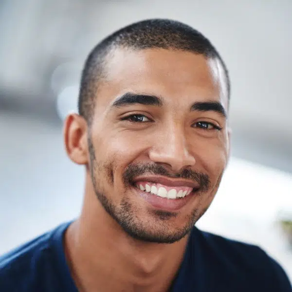 Smiling man in blue shirt in bright dental office setting, professional headshot.