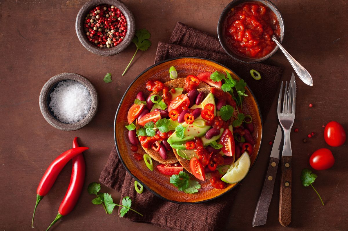 Colorful stir-fried vegetables with red peppers, tomatoes, and herbs in a wok on brown surface.