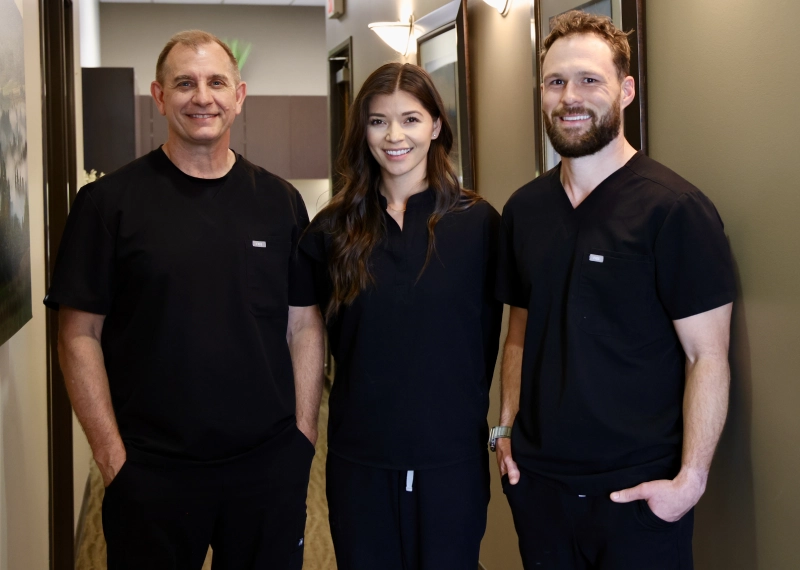 Three dental team members in dark scrubs standing together in a clinical hallway at Murray Scholls Family Dental.
