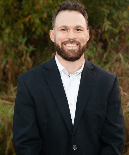 Professional headshot of Dr. Nicolas Maxim, cosmetic dentist in Beaverton, Oregon, smiling outdoors in a navy blazer.