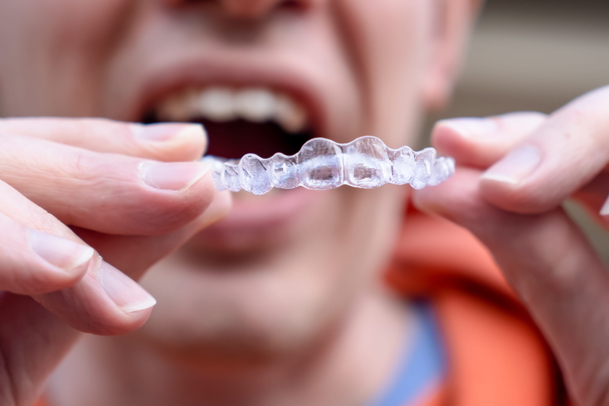 Patient holding clear Invisalign retainer after orthodontic treatment in Beaverton.
