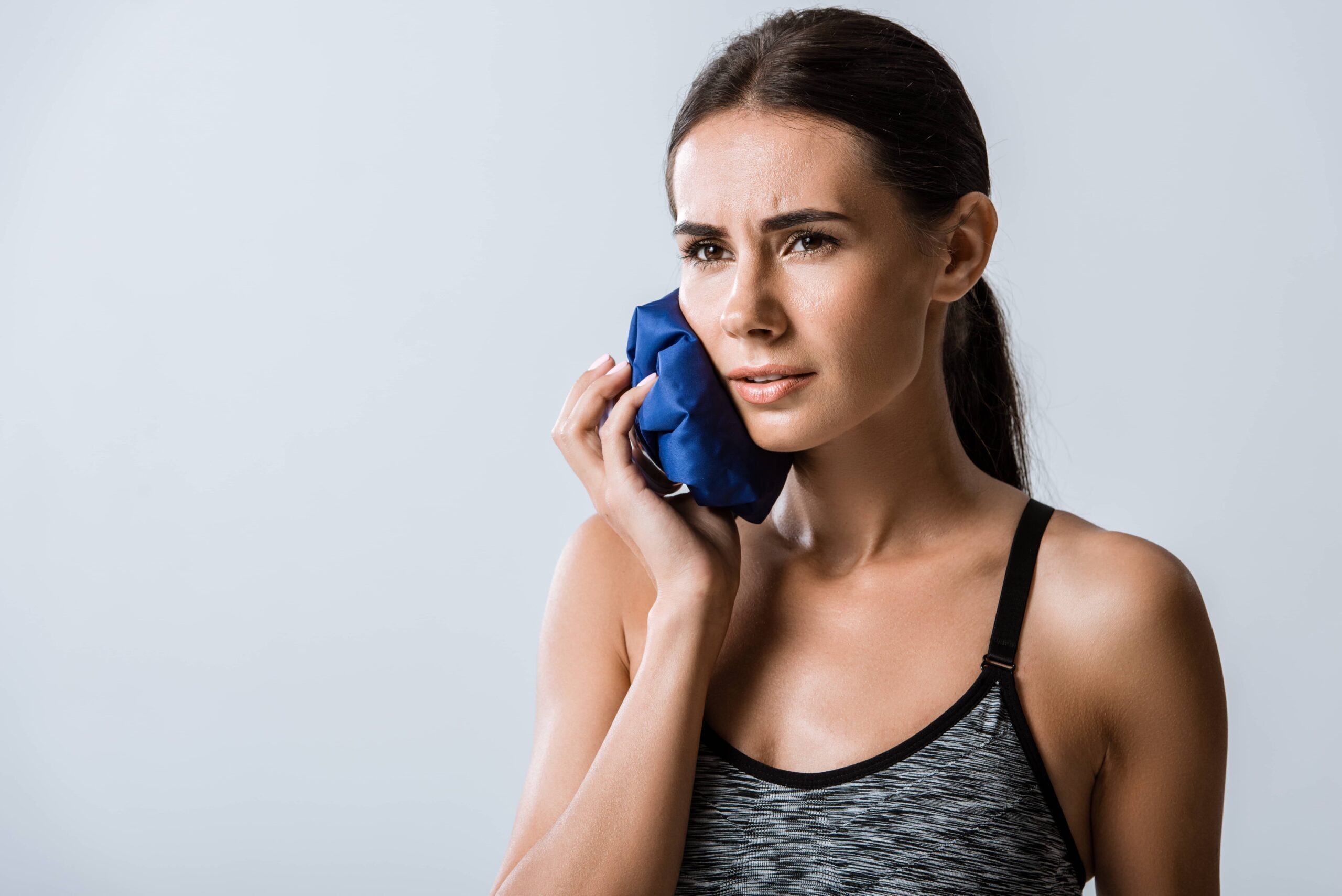 Woman holding ice pack to cheek for tooth pain relief after dental injury.